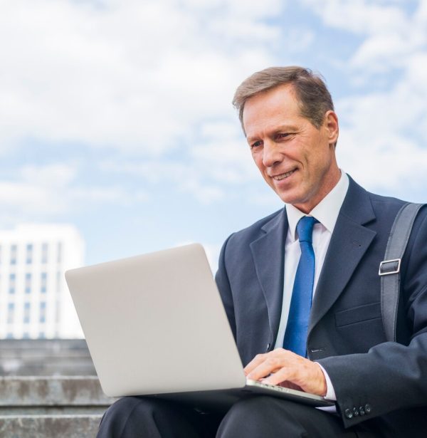 smiling-mature-businessman-using-laptop-outdoors_23-2147955325